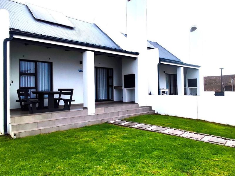 A well-maintained rear exterior view featuring a covered patio, built-in braai, and a neat garden with a paved walkway.