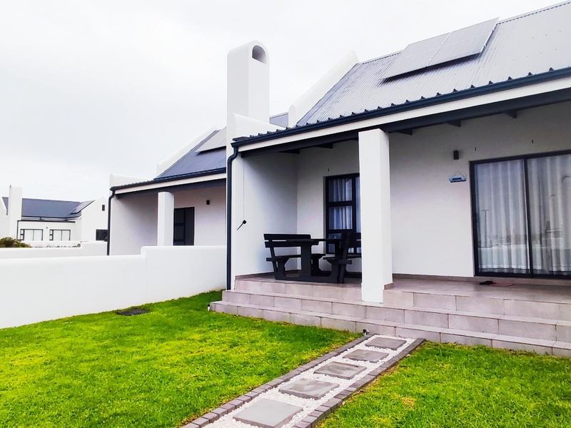 A well-maintained rear exterior view featuring a covered patio, tiled flooring, a white boundary wall, and a landscaped lawn area.