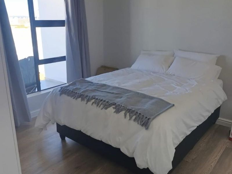 A bright bedroom featuring modern wood-look flooring and a large window providing natural light and access to an outdoor area.