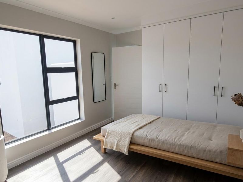 A bright, modern bedroom featuring built-in floor-to-ceiling wardrobes, sleek dark-framed windows, and durable wood-look flooring.