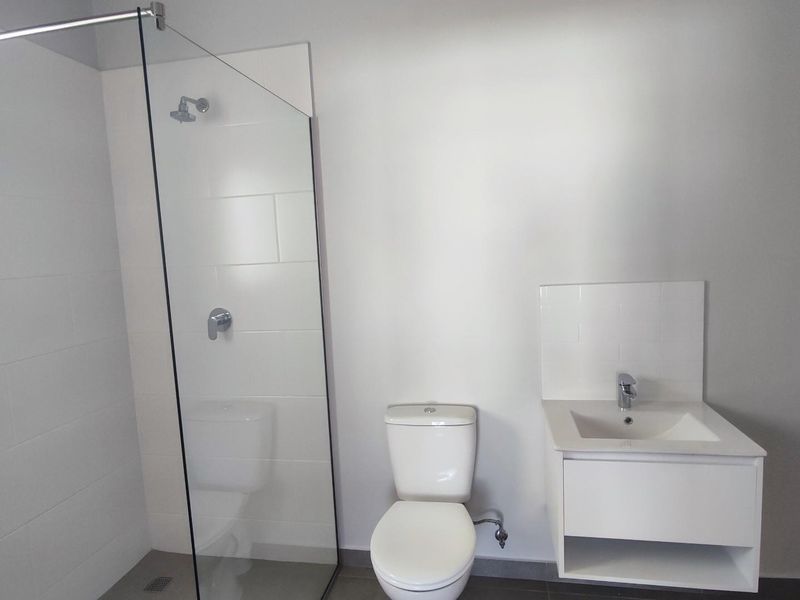 A modern, minimalist bathroom featuring a glass-enclosed walk-in shower, a wall-mounted vanity with a basin, and a white toilet.