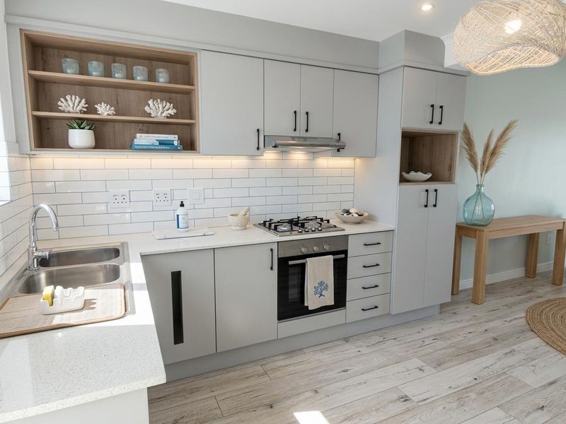 Modern open-plan kitchen featuring light grey cabinetry, stone countertops, subway tile backsplash, built-in gas hob, oven, and integrated extractor fan.