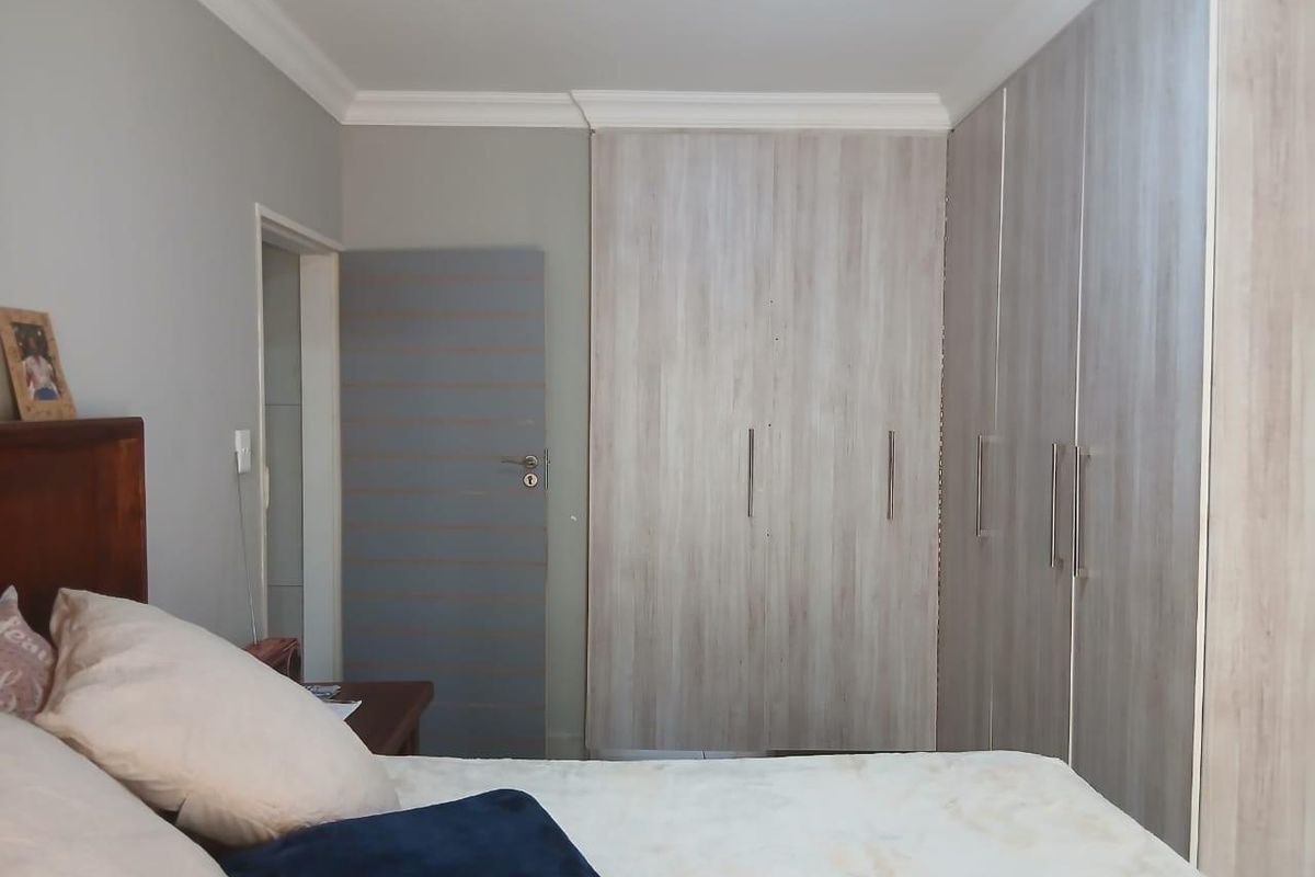 A well-maintained bedroom featuring modern wood-grain built-in cupboards and classic ceiling cornicing.