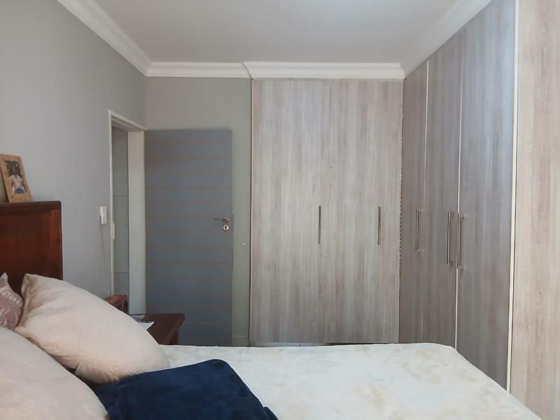 A well-maintained bedroom featuring modern wood-grain built-in cupboards and classic ceiling cornicing.