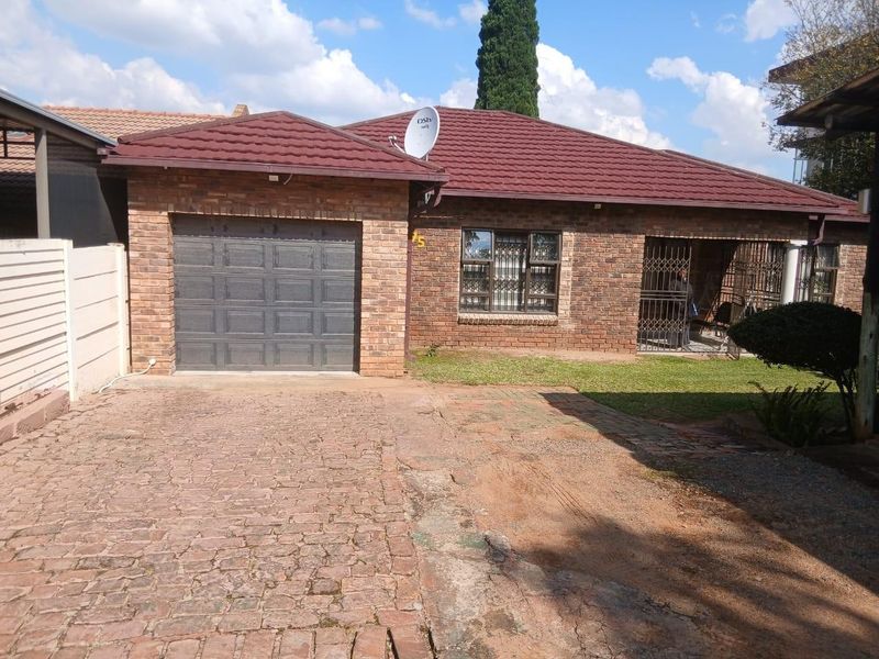 Front view of a facebrick house featuring a single garage, tiled roof, and paved driveway with security gates at the entrance.