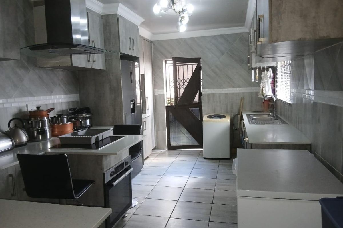 A functional kitchen featuring modern grey cabinetry, tiled finishes, built-in oven and hob, and direct access to an exterior area via a security door.