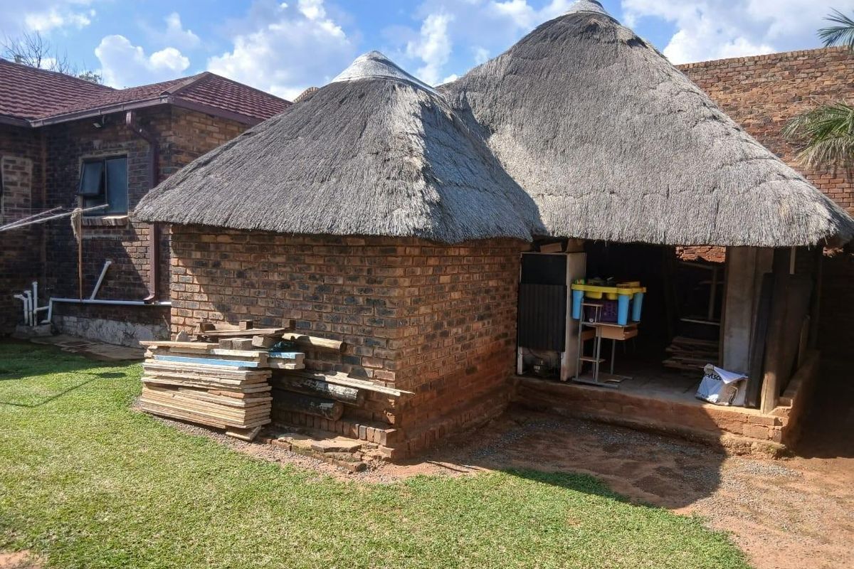 A rear view of a traditional thatched-roof structure with exposed brick walls, situated in a residential garden setting.