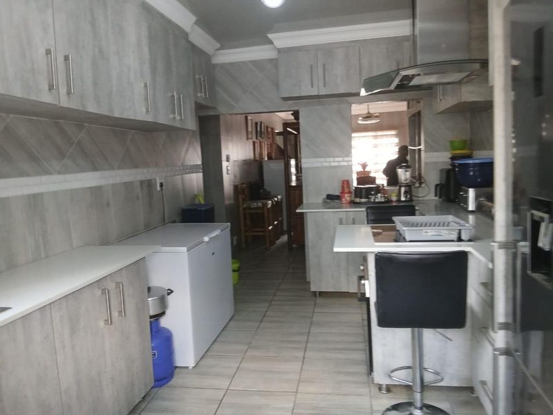 A functional kitchen featuring modern grey wood-look cabinetry, tiled backsplash, and tiled flooring, providing ample storage and workspace.