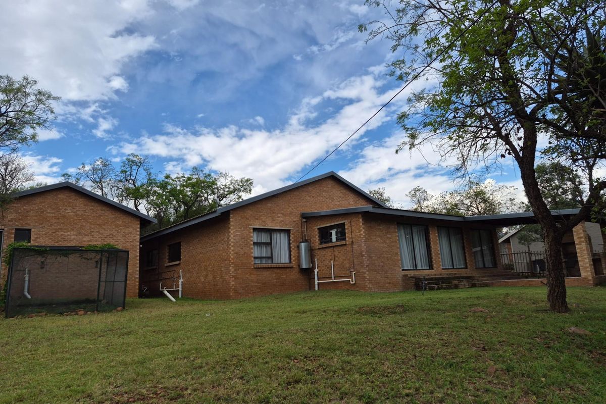 A view of the rear brick facade of the house, featuring large windows, a covered patio area, and a spacious surrounding garden.