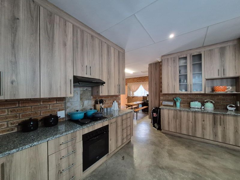 A functional kitchen featuring wood-look cabinetry, granite countertops, a built-in oven, and a hob with an extractor fan, set against a rustic brick backsplash.