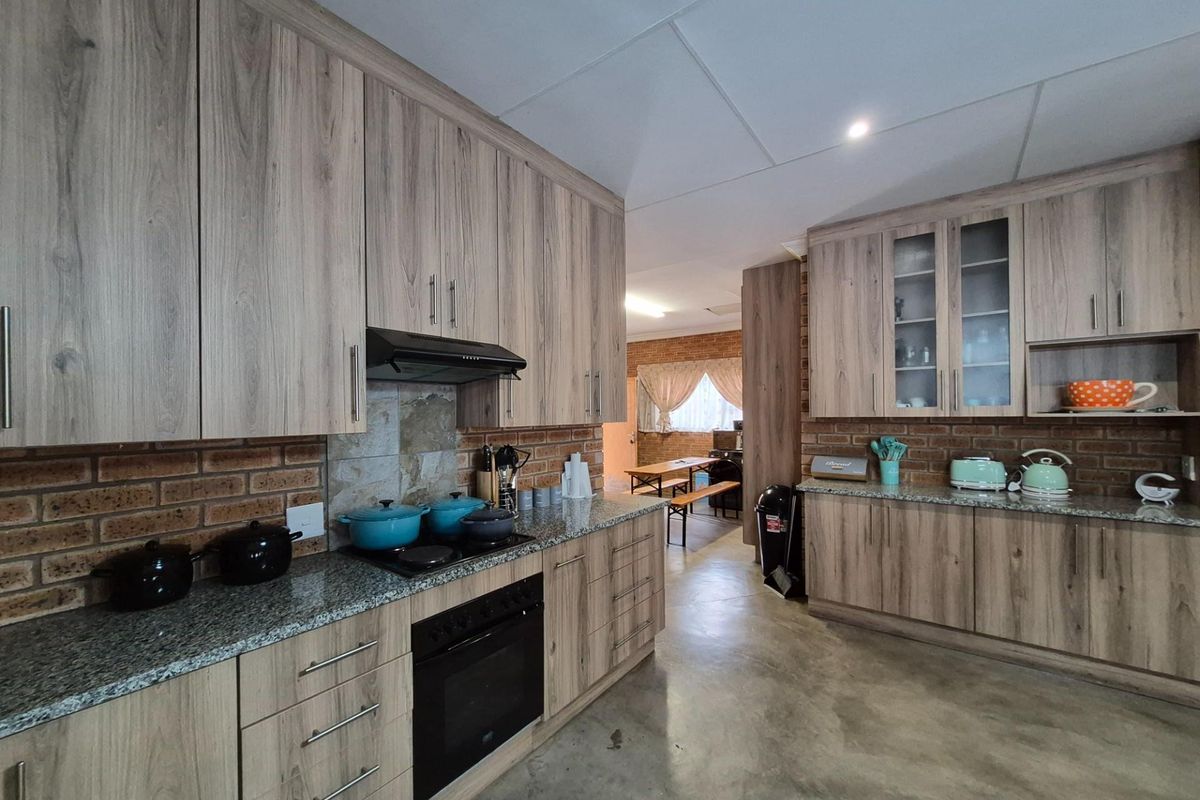 A functional kitchen featuring wood-look cabinetry, granite countertops, a built-in oven, and a hob with an extractor fan, set against a rustic brick backsplash.