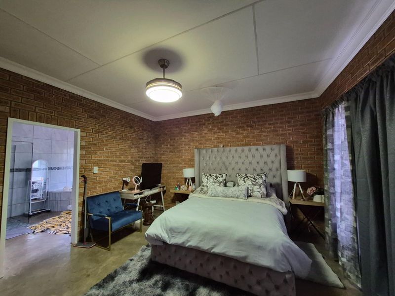 Spacious bedroom featuring exposed brick walls, a ceiling fan with integrated lighting, and direct access to an en-suite bathroom.