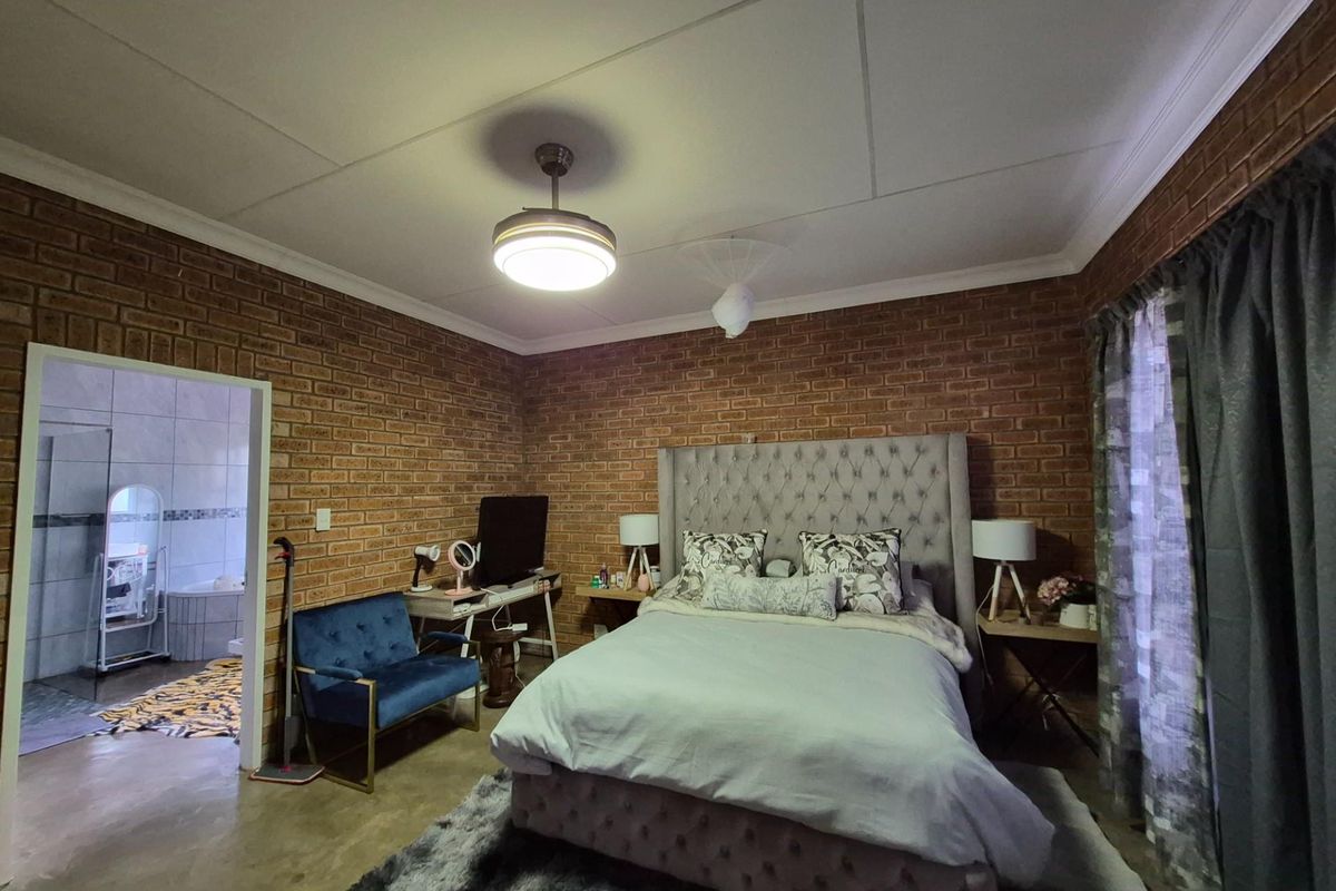Spacious bedroom featuring exposed brick walls, a ceiling fan with integrated lighting, and direct access to an en-suite bathroom.