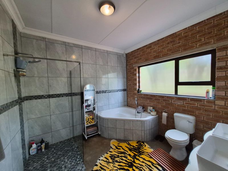 A bathroom featuring a corner bathtub, a walk-in shower with glass enclosure, a toilet, and a vanity, finished with exposed brick and tiled walls.