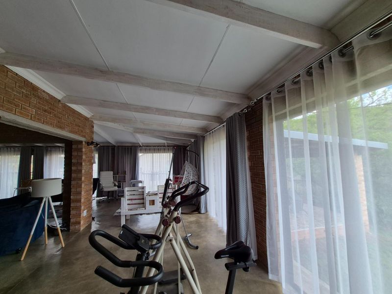Spacious open-plan living area featuring exposed timber ceiling beams, face-brick walls, and large windows providing ample natural light and garden access.
