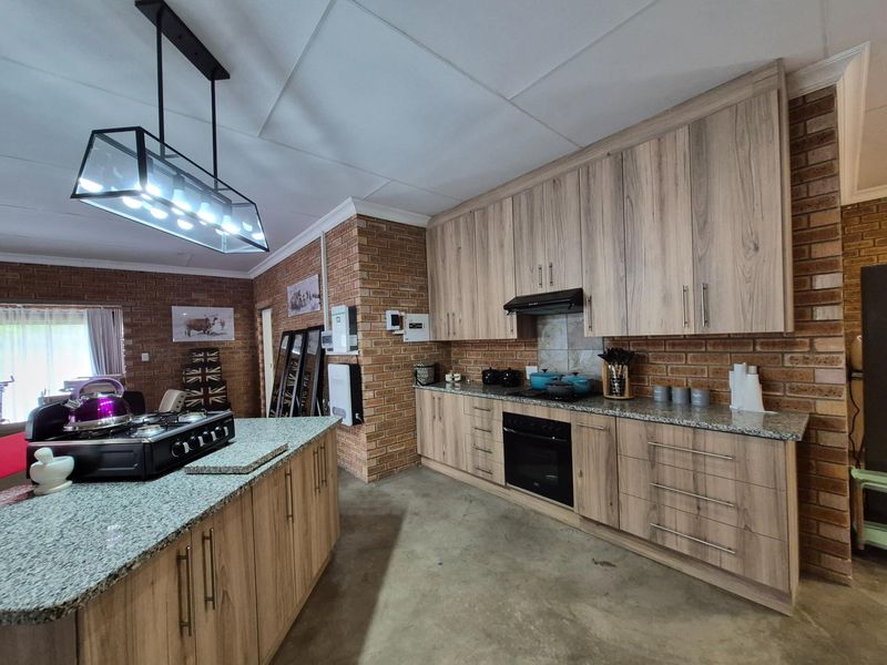 Modern kitchen featuring wood-grain cabinetry, granite countertops, a central island with a gas hob, and exposed brick walls.