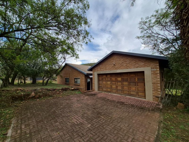 Exterior view of a brick-faced house featuring a double garage, paved driveway, and surrounding mature trees in a natural setting.