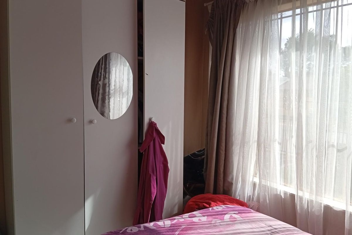 A bedroom featuring a built-in wardrobe with a circular mirror detail and a window fitted with security bars.