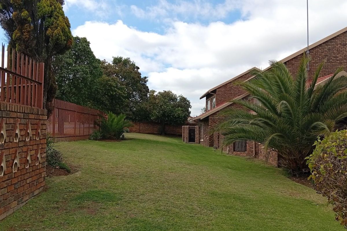 A spacious rear garden area featuring a well-maintained lawn, brick perimeter wall with security fencing, and views of the townhouse exterior.