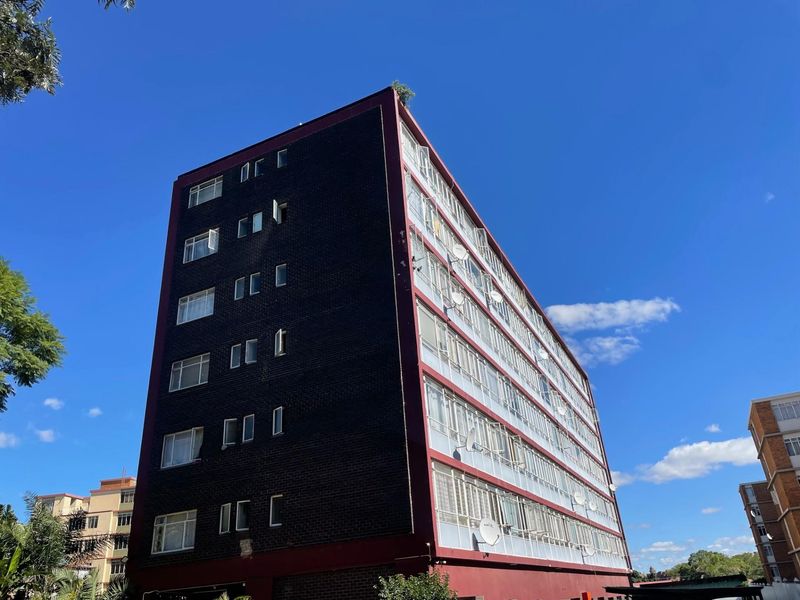 A multi-story apartment building exterior featuring dark brickwork and extensive window glazing under a clear blue sky.