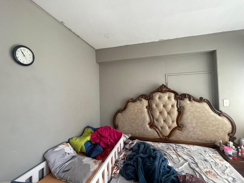 A bedroom featuring neutral grey walls and a ceiling showing signs of wear and paint deterioration.