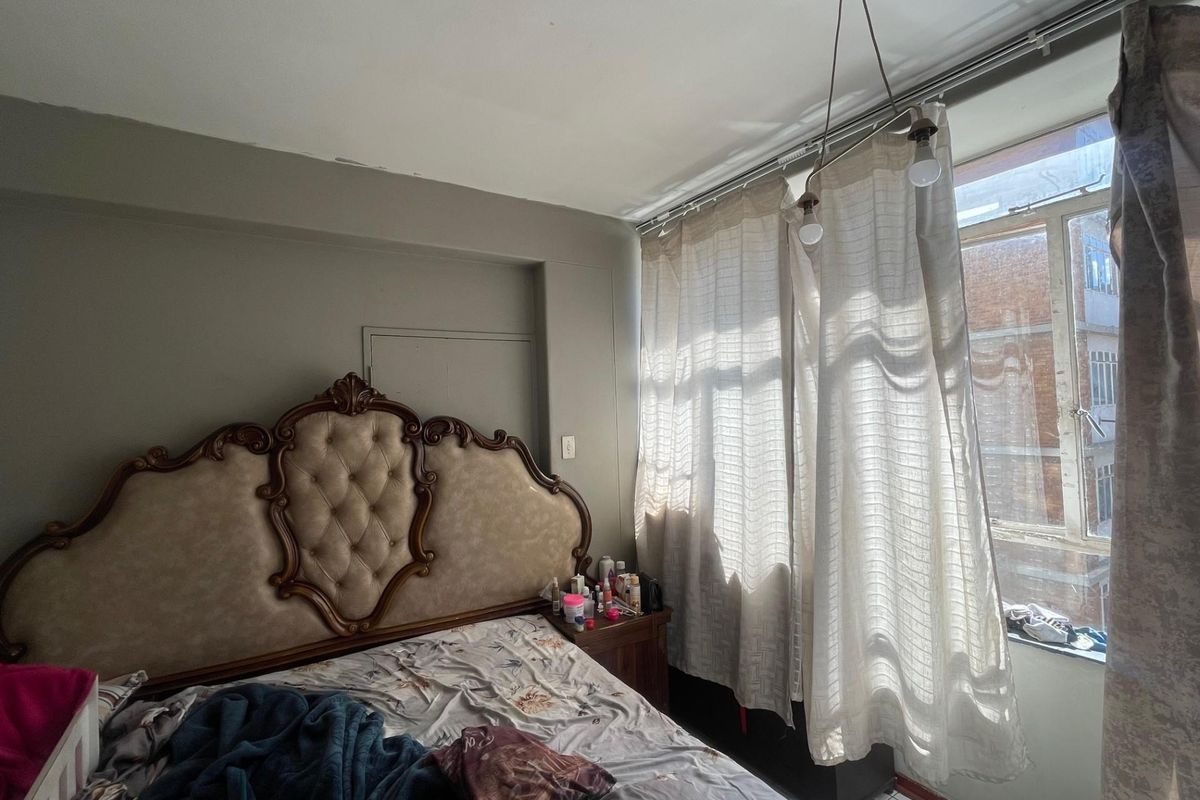 A bedroom featuring a window with curtain tracks and a ceiling-mounted light fixture, showing signs of minor wear on the ceiling.
