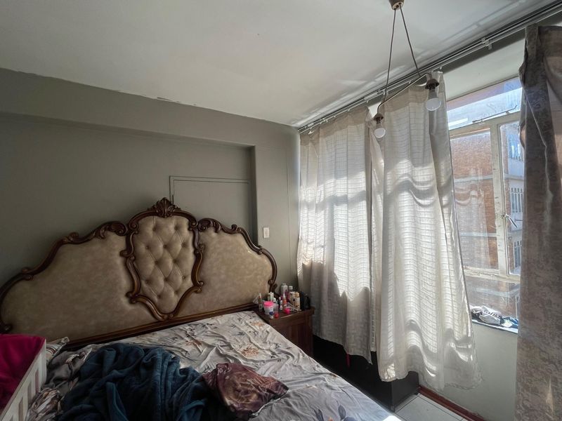 A bedroom featuring a window with curtain tracks and a ceiling-mounted light fixture, showing signs of minor wear on the ceiling.