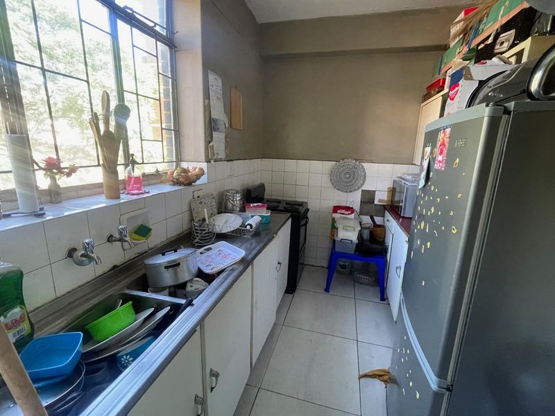 A compact kitchen featuring a double basin sink, tiled splashback, and built-in cabinetry, requiring cosmetic updates to improve its overall condition.