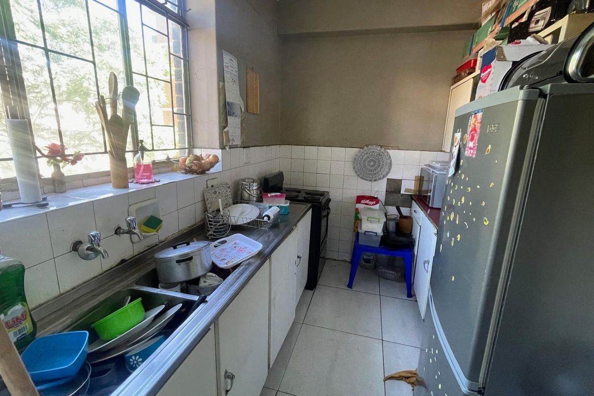 A compact kitchen featuring a double basin sink, tiled splashback, and built-in cabinetry, requiring cosmetic updates to improve its overall condition.