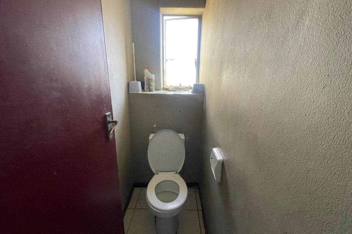 A compact, functional bathroom featuring a standard toilet, tiled flooring, and a small window for natural light.