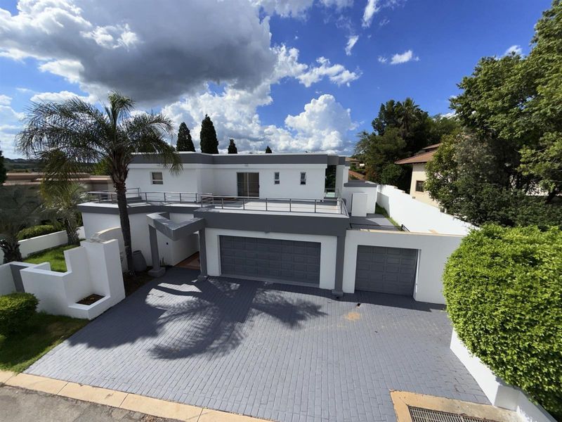 Modern double-story residence featuring a paved driveway, double garage, and a spacious upper-level balcony with metal railings.
