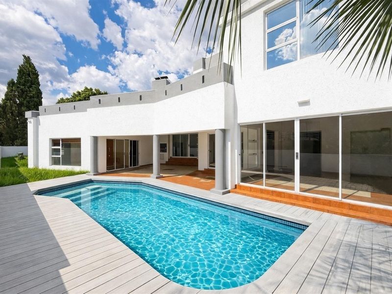 Rear exterior view featuring a swimming pool, composite decking, covered patio area, and large sliding glass doors leading into the home.