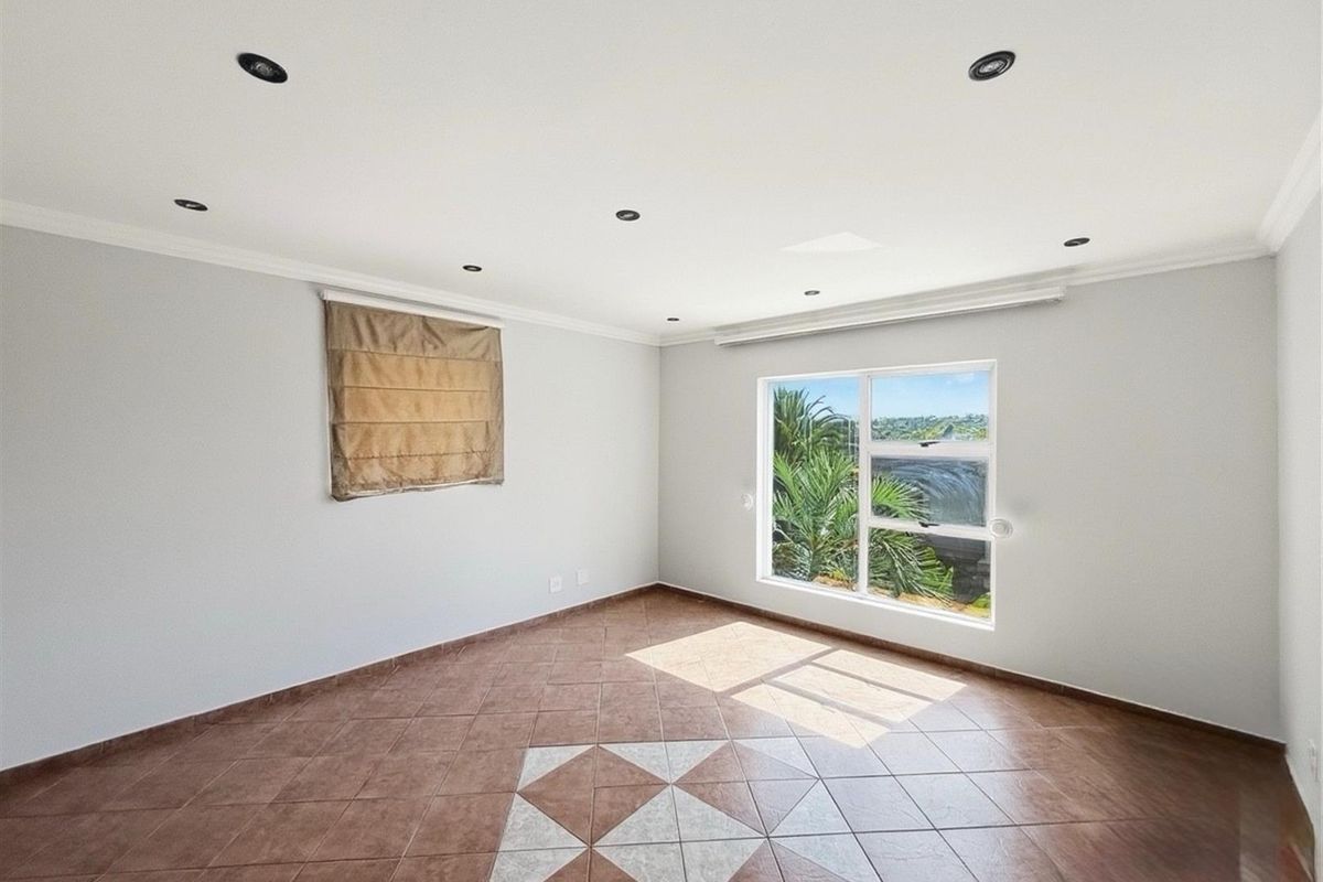 A bright, empty bedroom featuring tiled flooring with a decorative inlay, recessed ceiling lighting, and a window offering a view of the outdoors.