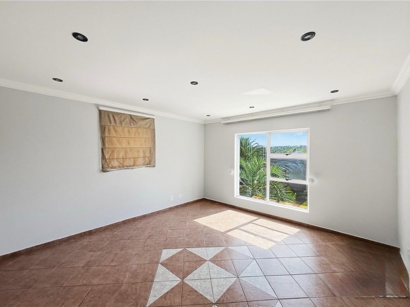 A bright, empty bedroom featuring tiled flooring with a decorative inlay, recessed ceiling lighting, and a window offering a view of the outdoors.