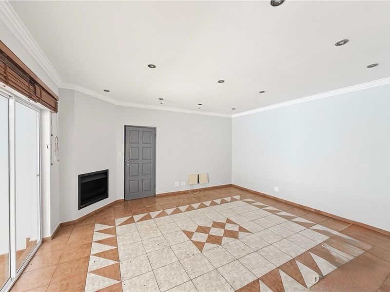 An empty living room featuring a built-in fireplace, tiled flooring with a decorative pattern, recessed ceiling lighting, and sliding glass doors leading outdoors.