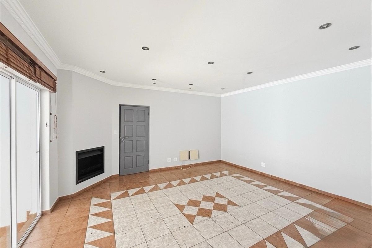 An empty living room featuring a built-in fireplace, tiled flooring with a decorative pattern, recessed ceiling lighting, and sliding glass doors leading outdoors.
