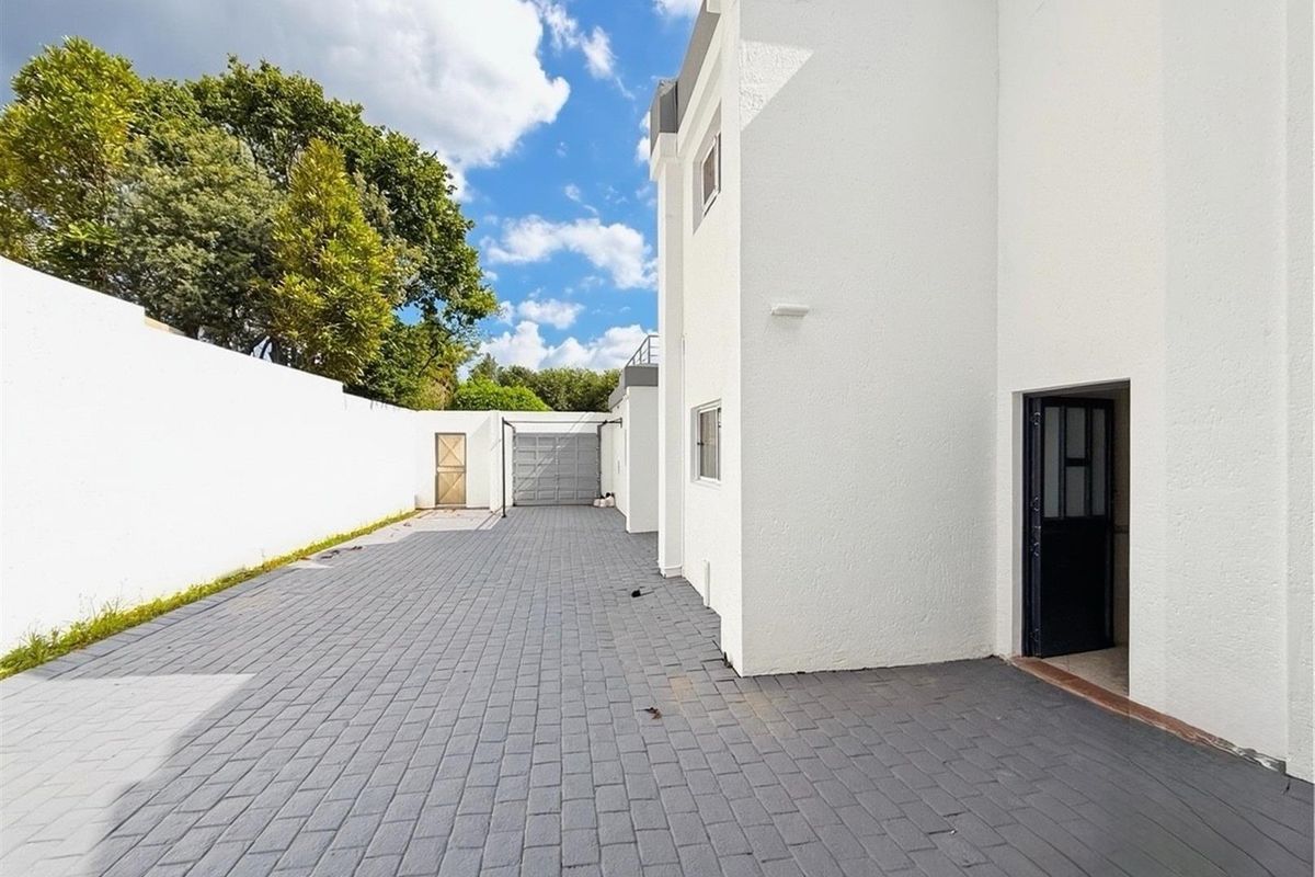 A paved side driveway and exterior access area featuring a white rendered facade, secure boundary wall, and a detached garage structure.