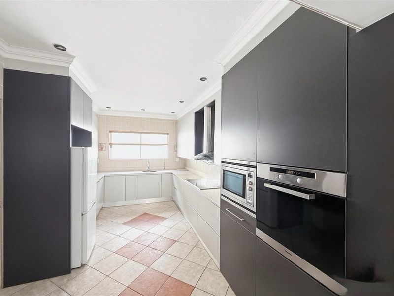 Modern kitchen featuring dark cabinetry, built-in oven and microwave, light-toned countertops, and tiled flooring with a decorative pattern.