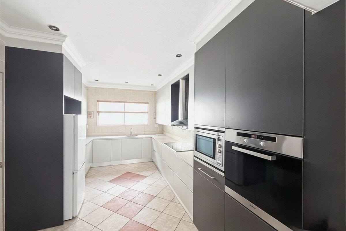 Modern kitchen featuring dark cabinetry, built-in oven and microwave, light-toned countertops, and tiled flooring with a decorative pattern.