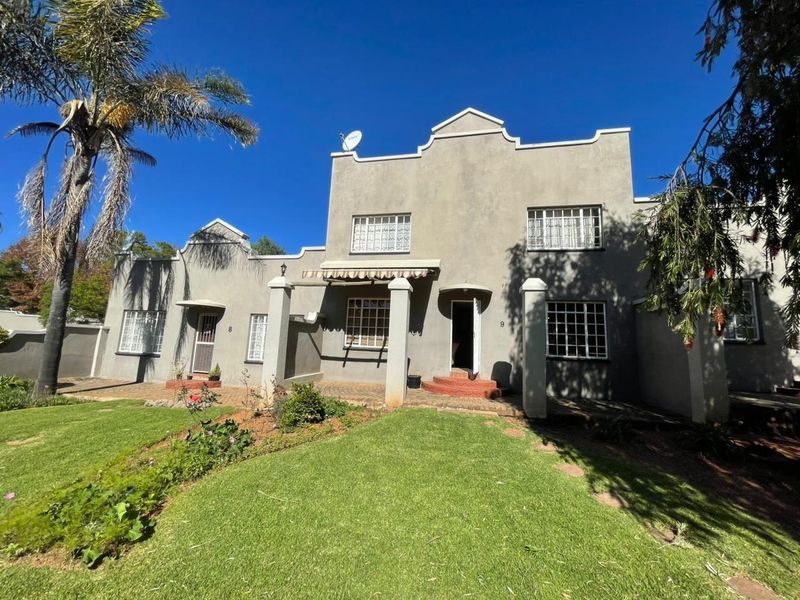 Front elevation of a townhouse complex featuring a classic architectural style, covered entrance porches, and a well-maintained front garden area.