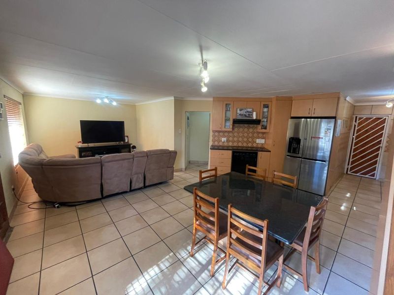 Open-plan living and dining area featuring tiled flooring and a functional kitchen with built-in cabinetry and integrated appliances.