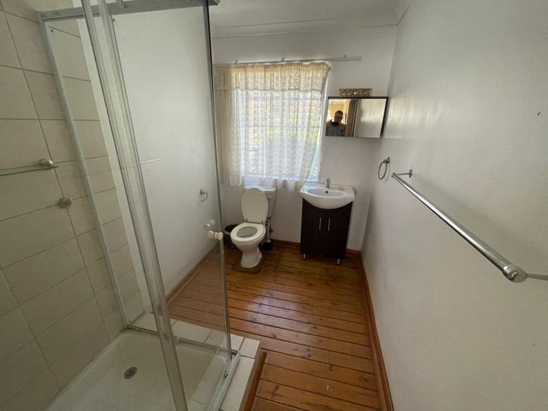 A functional bathroom featuring a glass-enclosed shower, a pedestal vanity, and a toilet, finished with timber flooring and neutral wall tones.