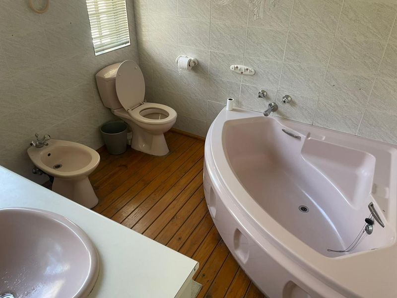 A dated bathroom featuring a corner bathtub, bidet, toilet, and vanity basin with timber flooring and wall tiling.