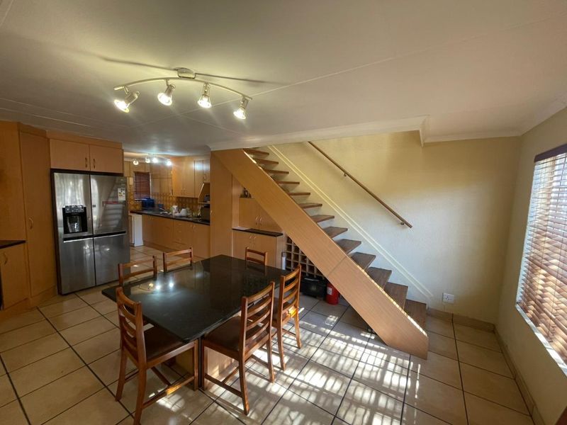 Open plan kitchen and dining area featuring wooden cabinetry, tiled flooring, and a staircase with a wooden handrail.
