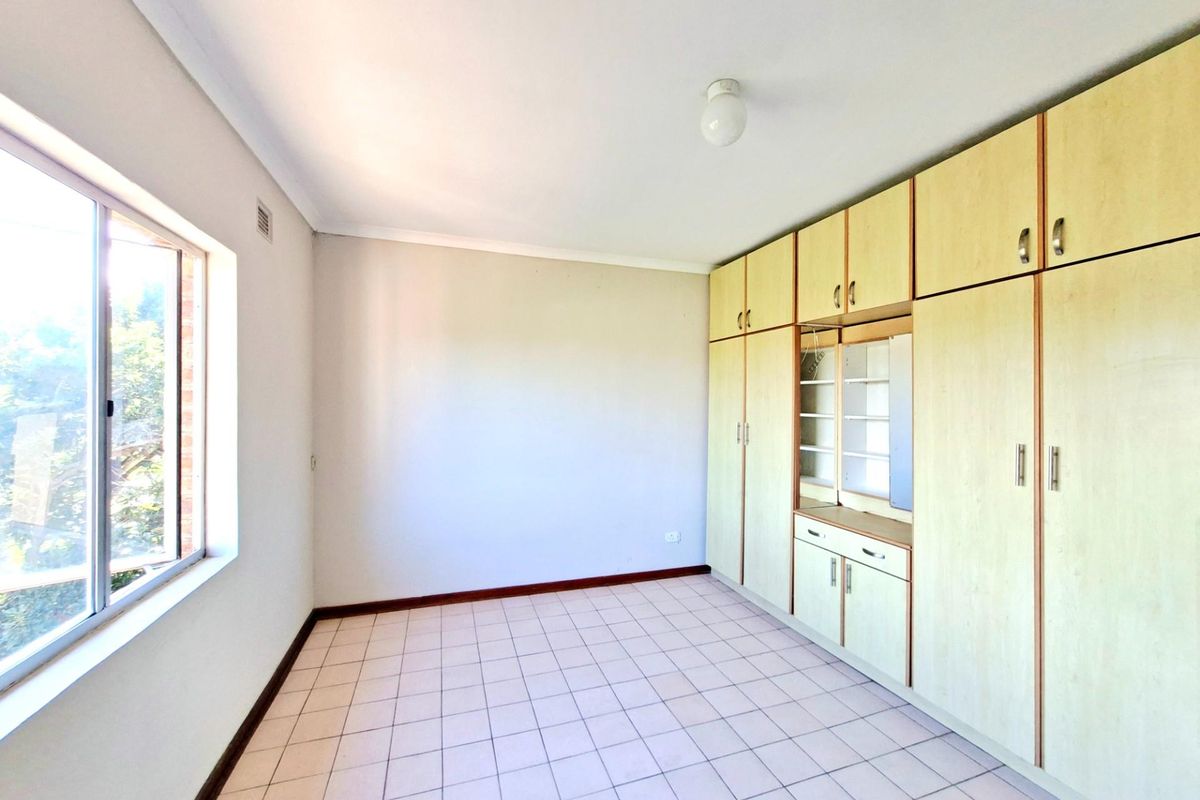 A bright, empty bedroom featuring built-in wooden cabinetry with integrated shelving and tiled flooring, offering a functional space ready for personalization.
