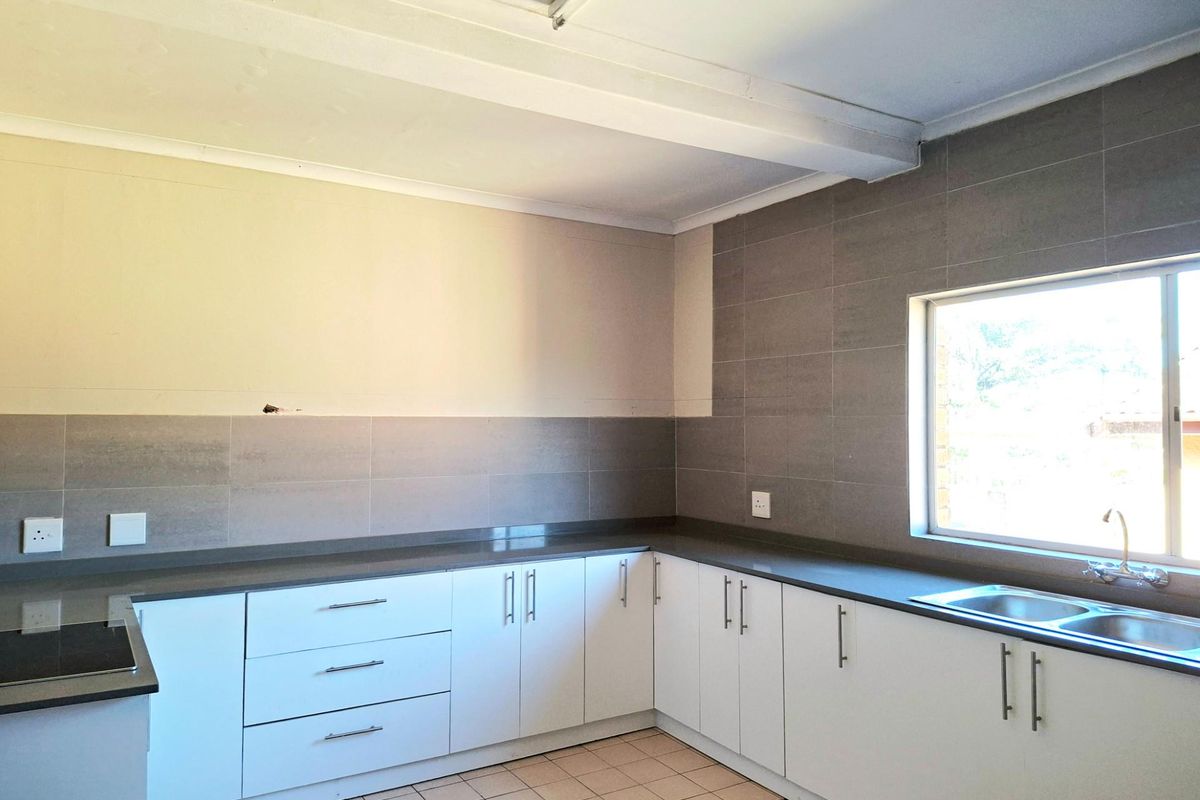 A functional kitchen featuring white cabinetry, dark stone-look countertops, tiled splashbacks, and a double stainless steel sink under a window.
