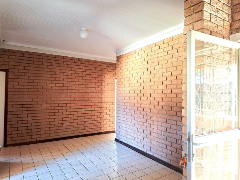 An empty interior space featuring exposed face-brick walls, tiled flooring, and a white tongue-and-groove ceiling, providing a neutral foundation for living or dining areas.