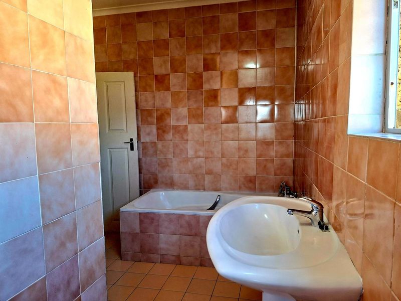 A dated bathroom featuring full-height wall tiling, a built-in bathtub, and a pedestal basin.