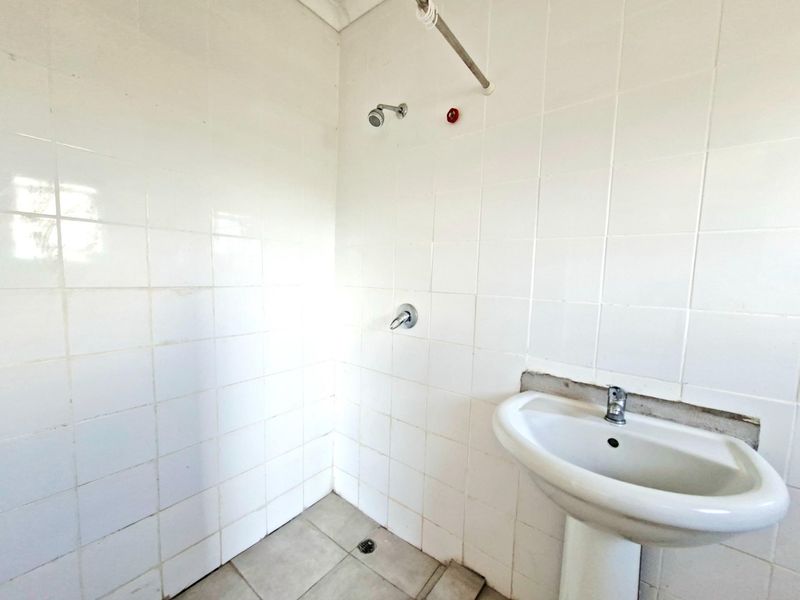 A basic bathroom featuring a pedestal basin and shower area with white wall tiles and floor tiling.