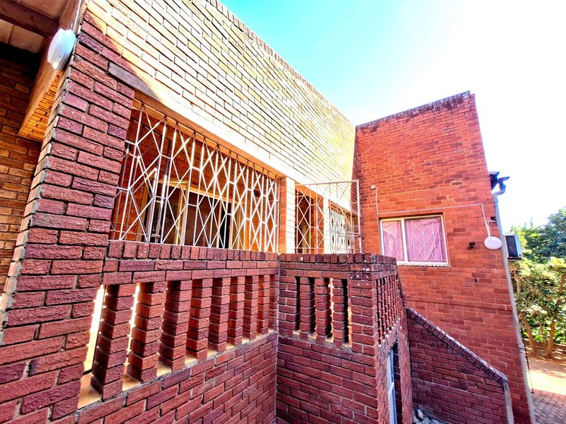 Exterior view of a red brick house featuring a raised terrace with brick balustrades and metal security grilles on the windows.